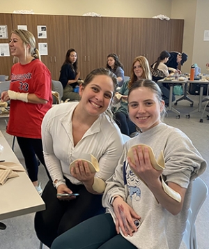 Two young people hold items in their hands while sitting in a classroom